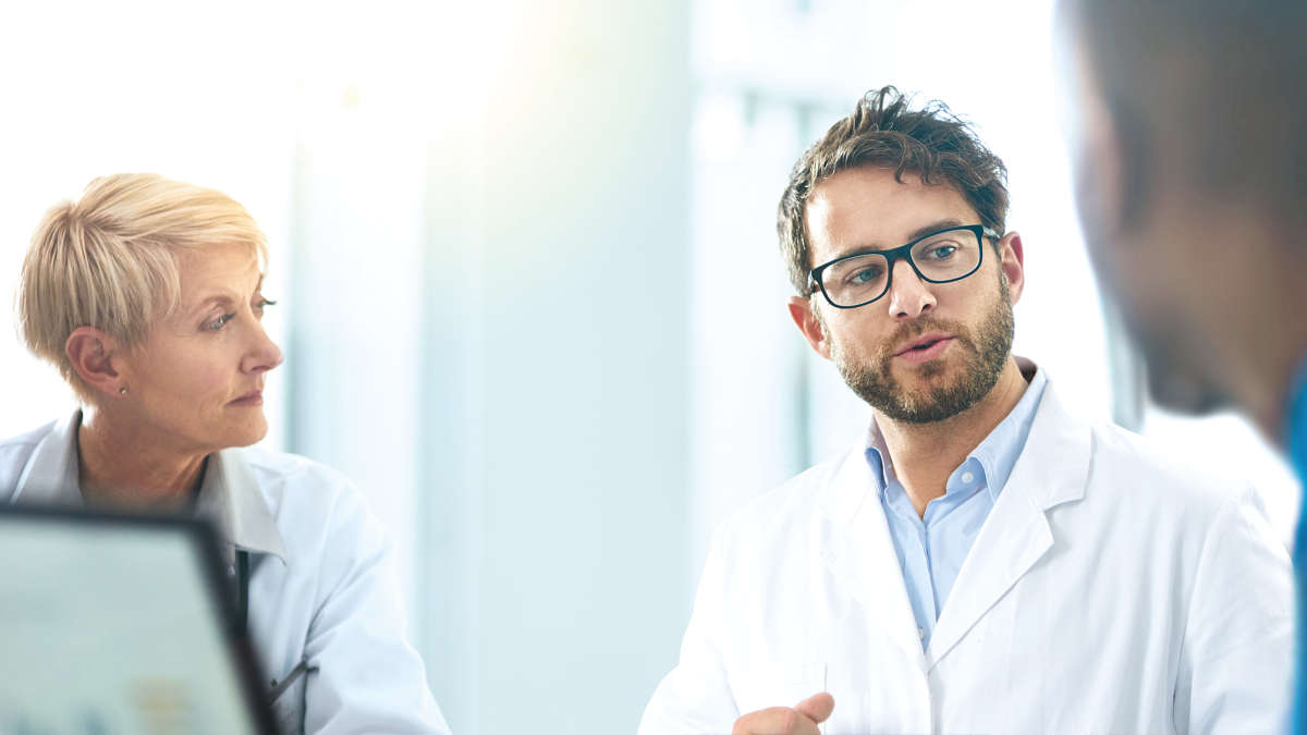 Enabling your cancer research from discovery to actionable insight, three people, discussing, sitting around a table, wearing a labcoat, team